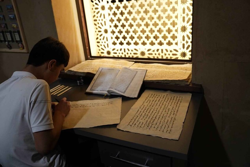 A person writing at a desk with papers and an open book. 3