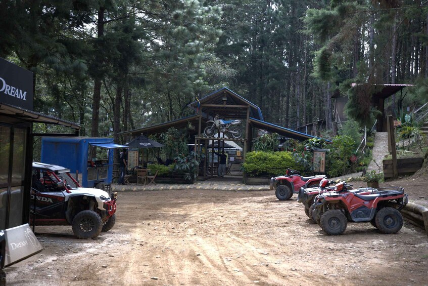 A dirt road leading to a wooden cabin with ATVs parked nearby. 4