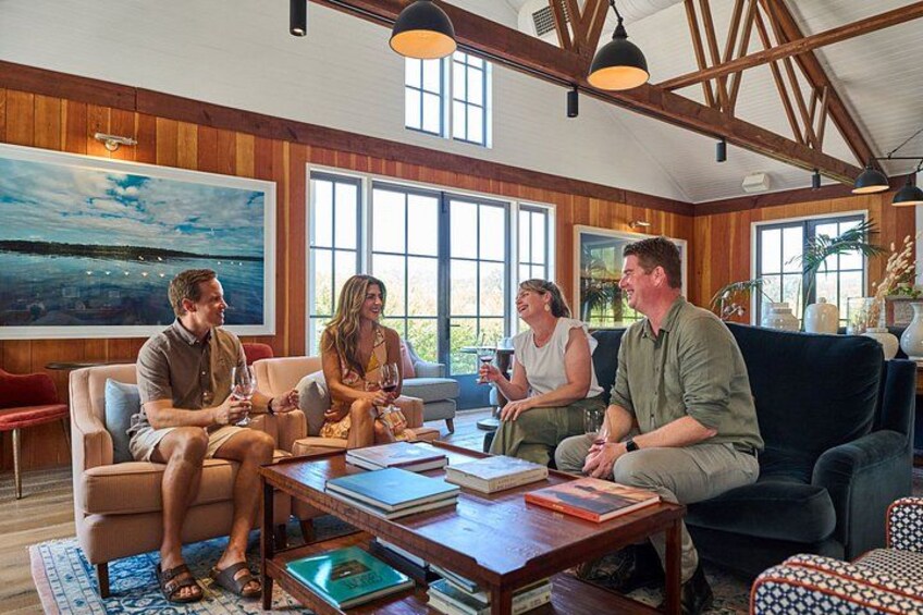 A group of people sitting on couches in a wooden-floored room with large windows. 5