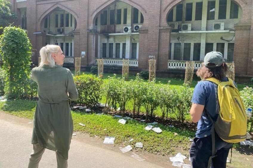 Due persone camminano su un sentiero di fronte a un edificio con finestre ad arco e pareti in mattoni. 2