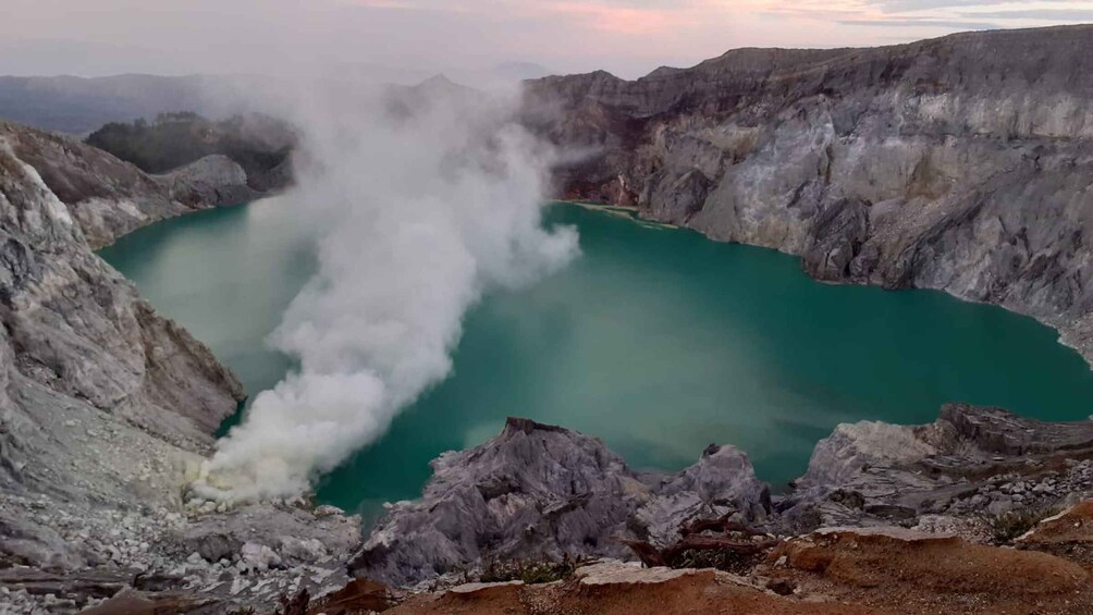 A geothermal area with a turquoise lake surrounded by rocky terrain and steam rising from the ground. 5