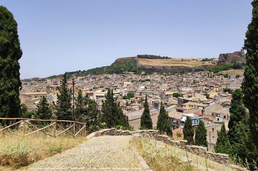 Une ville dominée par une colline imposante en arrière-plan, un sentier pavé qui y mène et des arbres dispersés. 3