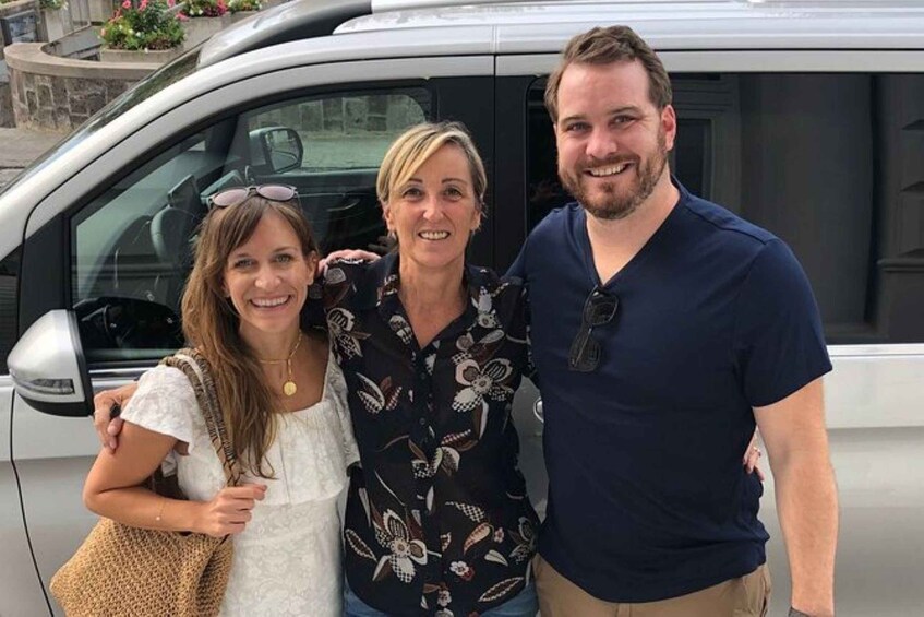 Three people standing in front of a vehicle. 2