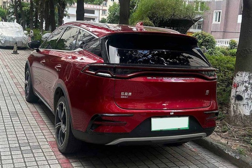 A red car parked on a brick pavement with trees and buildings in the background. 4