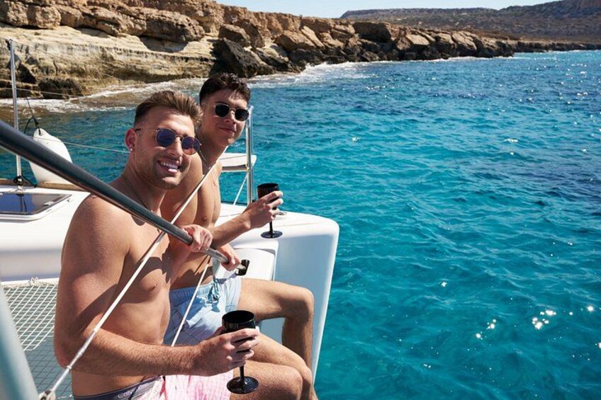 Two people on a boat in a clear blue sea with rocky cliffs in the background. 2