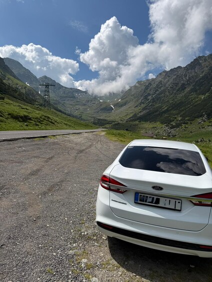 A white car parked on a gravel road with a mountainous landscape in the background. 4