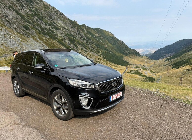 A black SUV parked on a gravel road with a mountainous landscape in the background. 3