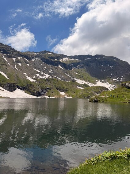 A mountain lake with snow patches, clear water, and a grassy shoreline. 3