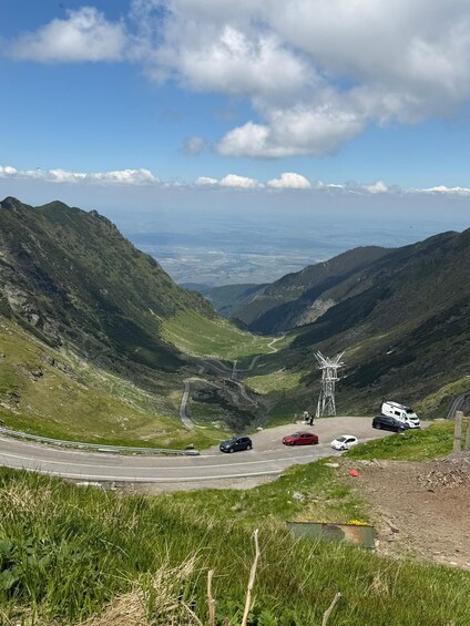 A winding mountain road with vehicles, a power line tower, and a valley in the distance. 2