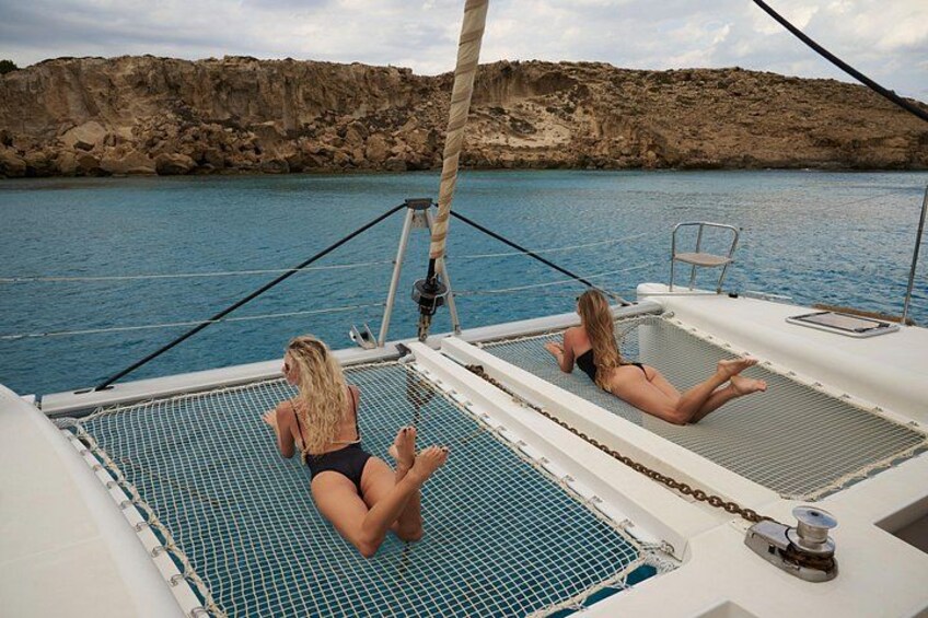Two people sunbathing on a boat with a rocky coastline in the background. 2