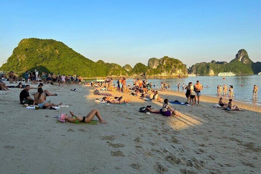 Ein belebter Strand mit Menschen, die sich sonnen und schwimmen, umgeben von grünen Hügeln und klarem Wasser. 5