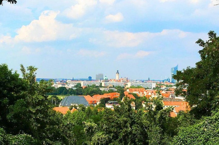 A cityscape with red-roofed buildings, a prominent tower, and a mix of greenery and urban development. 1