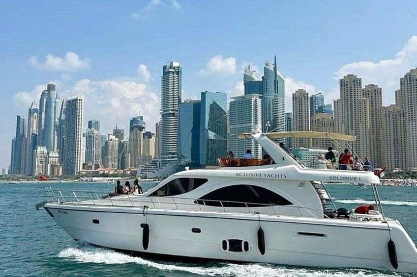 A white yacht named 'Xclusive Yachts' with a city skyline in the background. 1