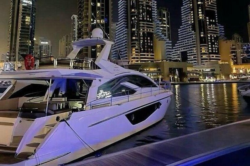 A white yacht docked at a marina with a city skyline in the background. 2