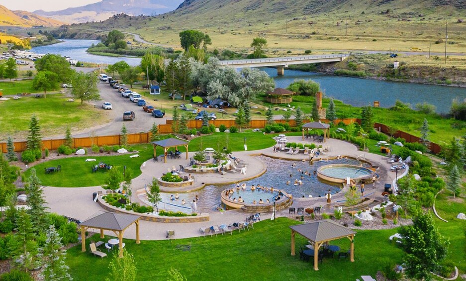 A resort with a swimming pool, outdoor seating, and a bridge over a river. 2