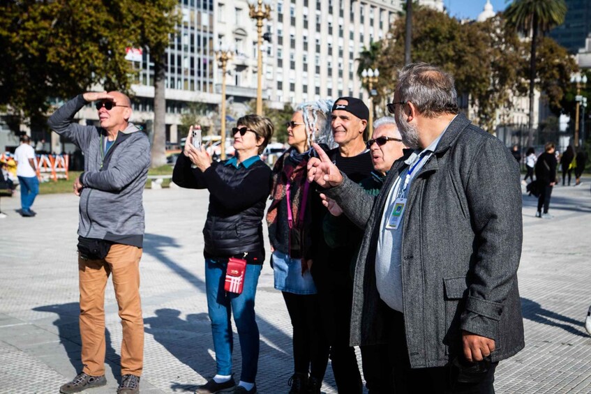 A group of people standing on a city sidewalk, some taking photos. 4