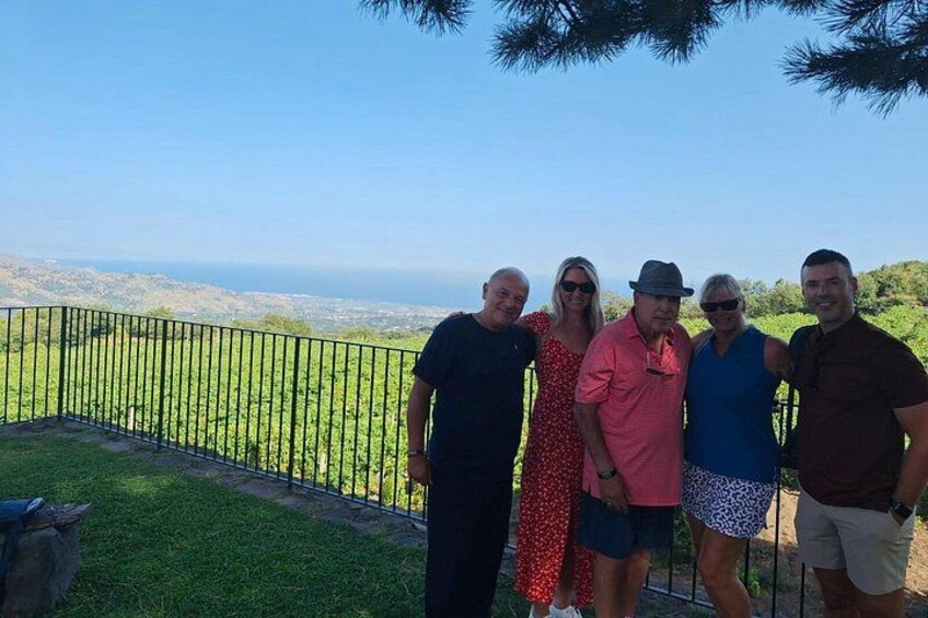 Eine Gruppe von Menschen steht auf einem Balkon mit Blick auf eine grüne Landschaft und das Meer. 4