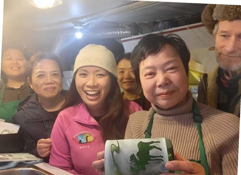 A group of people in a casual indoor setting, possibly a cafe or restaurant, with one person holding a mug with a green design. 4