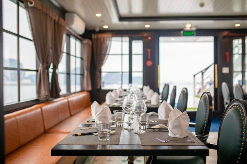 Un comedor con mesas dispuestas para el servicio, una cabina de cuero y ventanas amplias con cortinas. 3