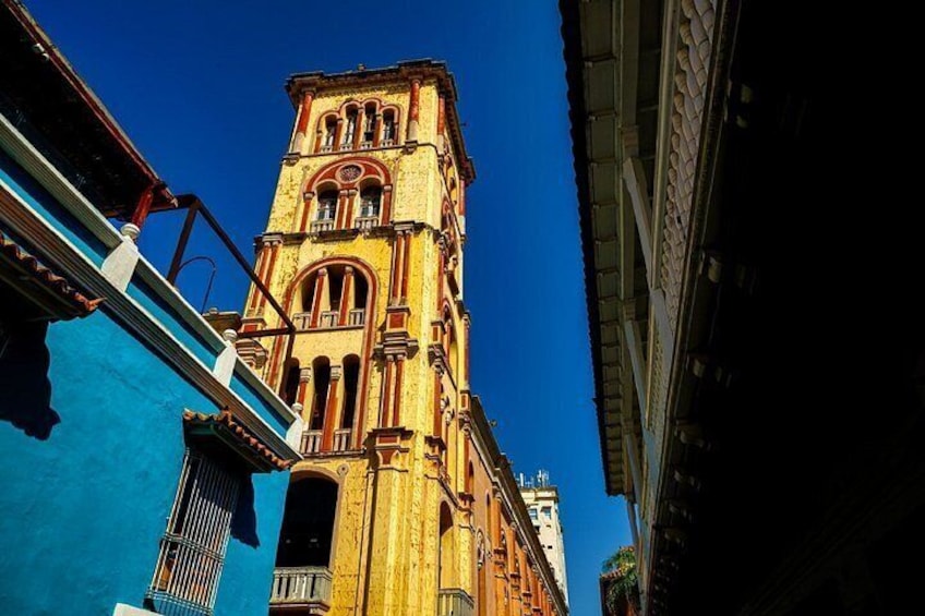 A tall, ornate tower with arched windows and a balcony, set against a clear blue sky. 2