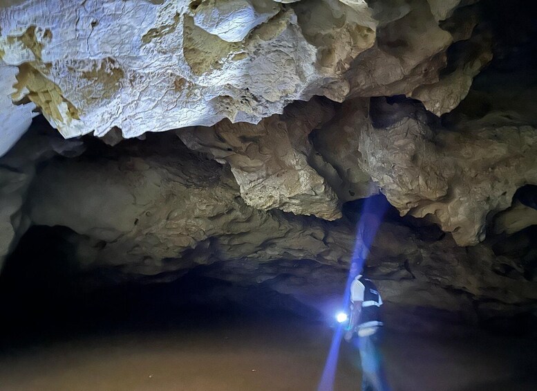 A cave interior with rough, uneven rock formations and a person holding a flashlight. 4