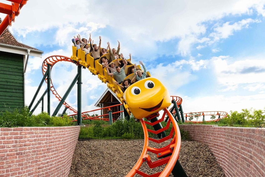 A roller coaster with a smiling face design, surrounded by greenery and a clear sky. 1