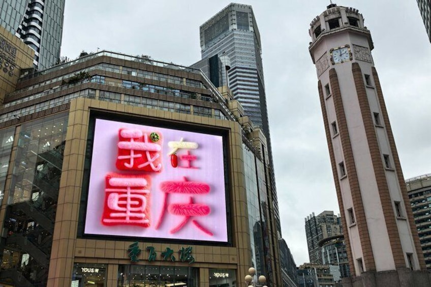Een groot digitaal reclamebord met Chinese karakters, een modern gebouw en een klokkentoren op de achtergrond. 1