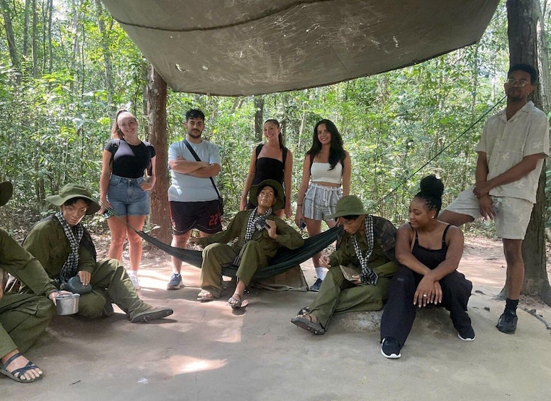 A group of people in a forested area with a concrete structure overhead. 1