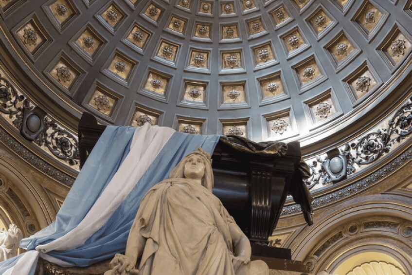 A domed ceiling with intricate gold decorations and a statue draped in blue and white cloth. 2