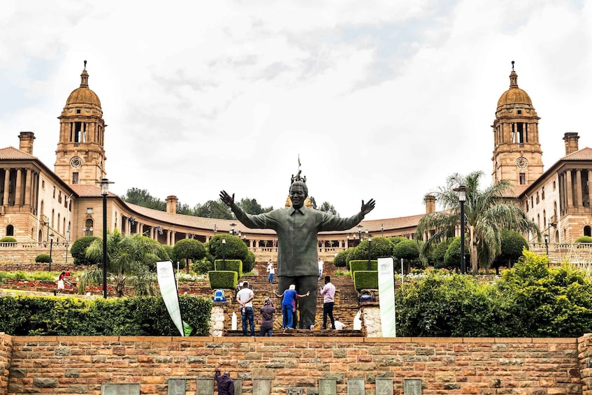 A large statue with outstretched arms in front of a historic building with two towers. 1