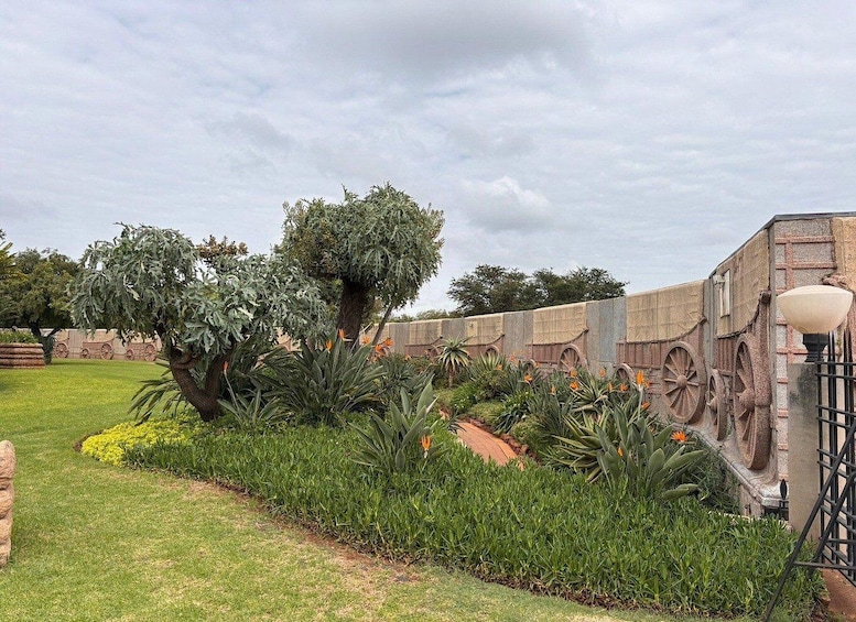 A garden with a large tree, a stone wall with decorative elements, and a street lamp. 5