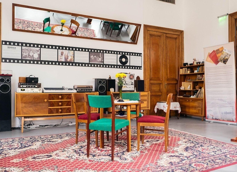 A room with a wooden cabinet, a table with chairs, a mirror, and a wall with a filmstrip and posters. 2