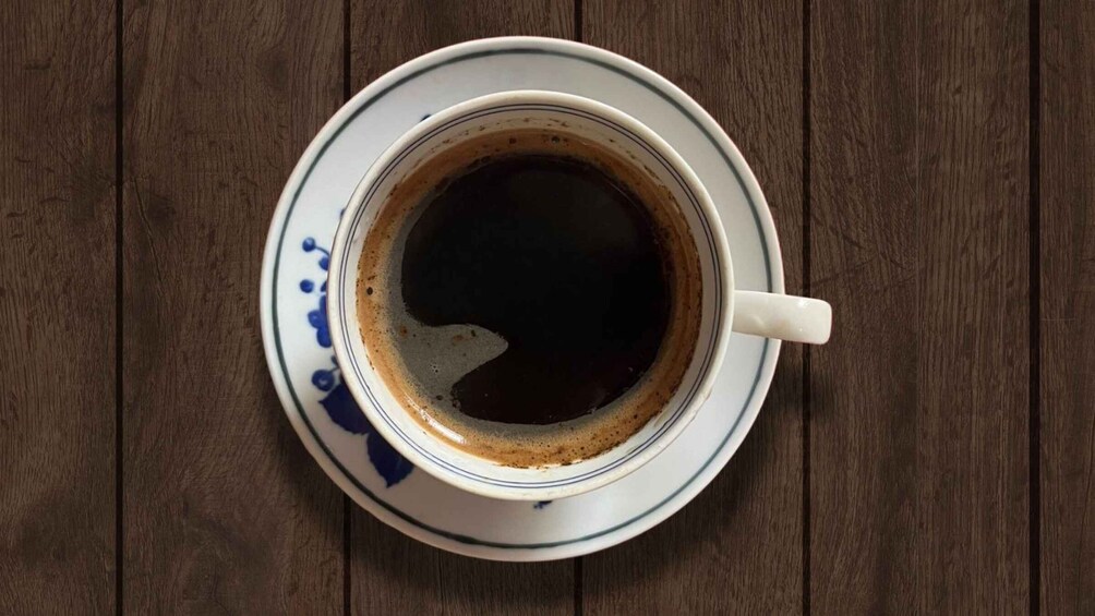 A cup of coffee on a saucer with a wooden table background. 1