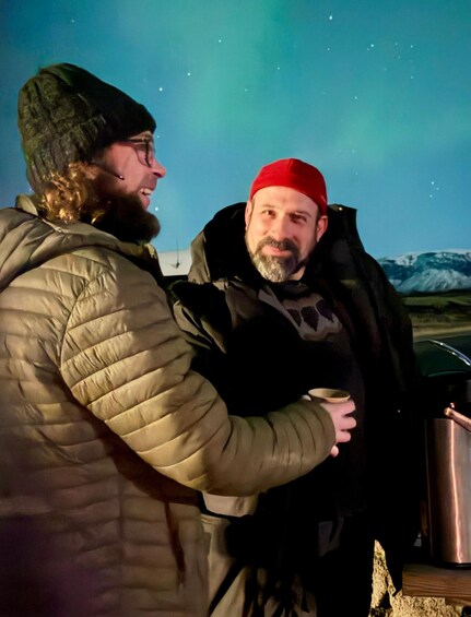 Zwei Personen draußen bei Nacht, eine trägt eine grüne Jacke, die andere eine schwarze Jacke mit rotem Hut. 3