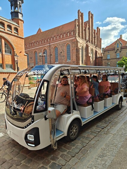 A city tour bus with passengers, parked in front of a historic building with a clock tower. 2