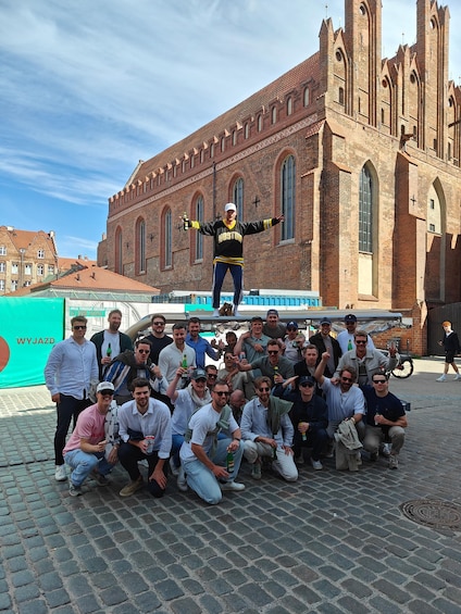 A group of people posing in front of a historic brick building with arched windows and a cross on the facade. 2