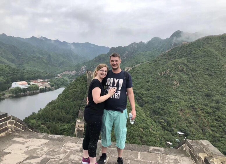 A couple standing on a stone wall overlooking a river and mountains. 2