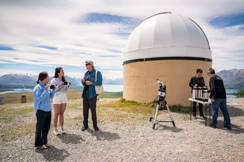 Un groupe de personnes se tient autour d’un grand dôme d’observatoire, avec des montagnes en arrière-plan. 4