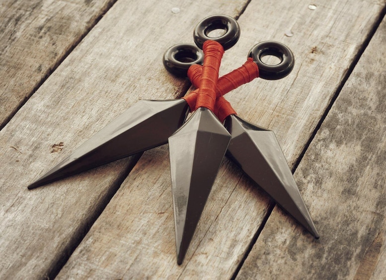 A pair of ninja scissors with three blades and a red handle on a wooden surface. 1
