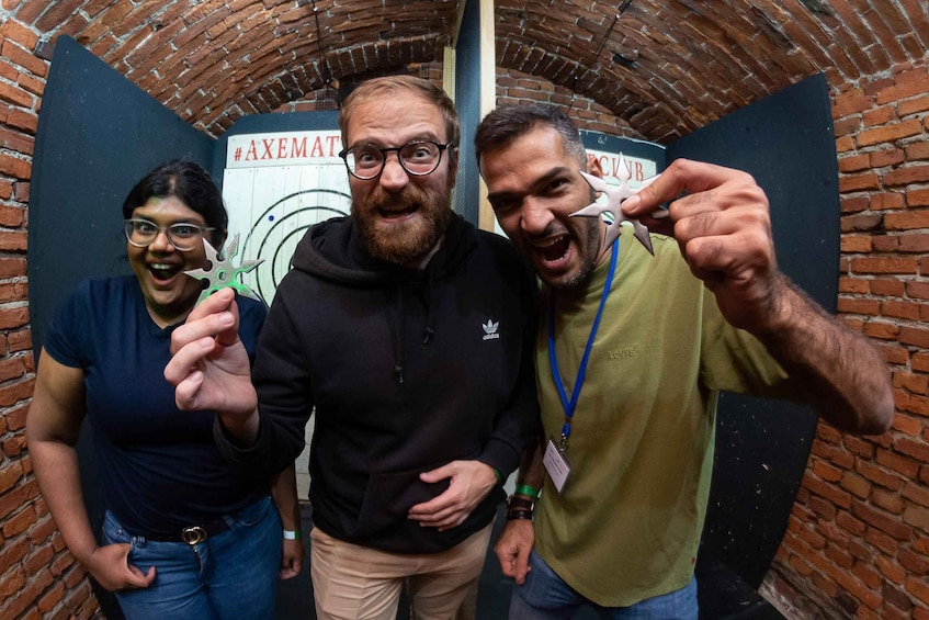 Three people in a brick-walled room with a sign reading "#AXEMAT". 3