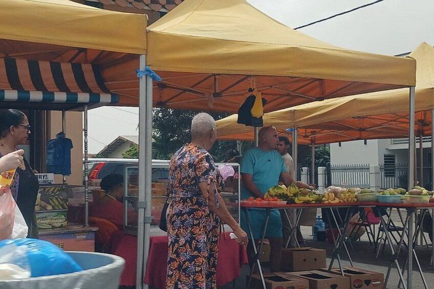A market stall with yellow canopies, a person in a patterned dress, and various fruits and vegetables. 3