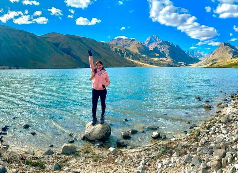 A person standing on a rock by a clear lake with mountains in the background. 5