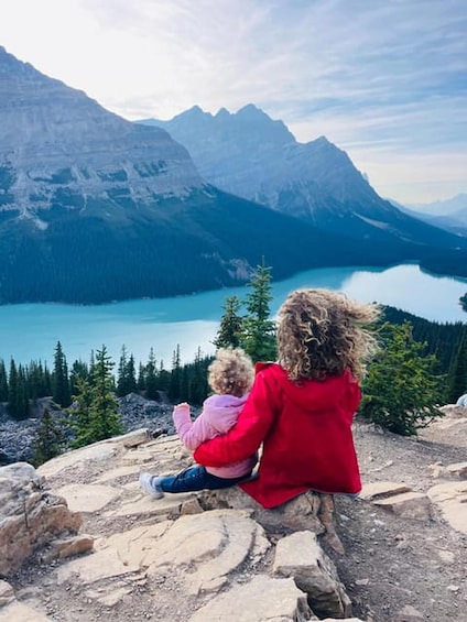 Two people sitting on a rocky outcrop overlooking a mountain lake. 2