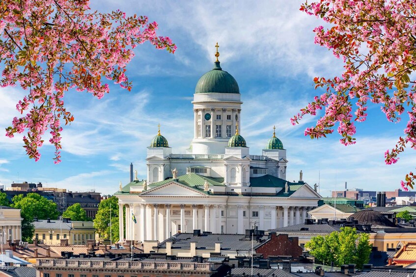A large white building with green domes and a tall tower, surrounded by trees and other buildings. 3