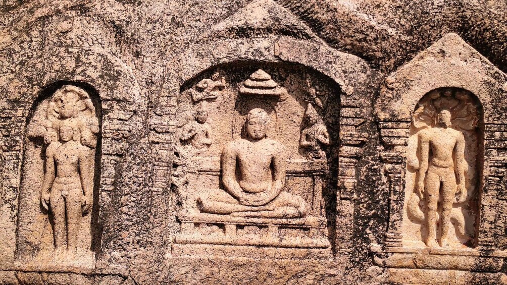 A rock-cut temple with three niches, each containing a statue: a standing figure, a seated figure, and a standing figure with a headdress. 4