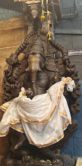 A detailed stone sculpture of a deity with multiple arms, draped in a white cloth with golden borders, and adorned with flowers. 2