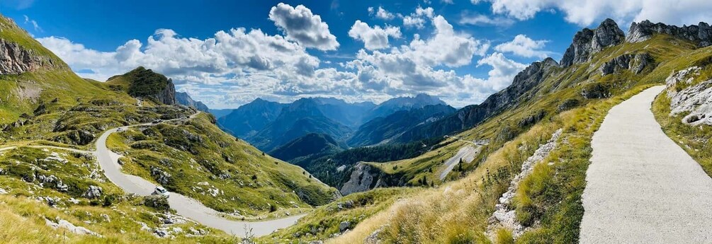 A winding mountain road surrounded by lush green hills and rocky outcrops under a clear blue sky. 4