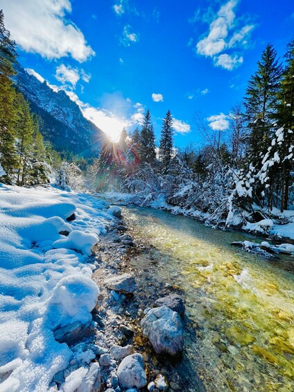 A snow-covered river flowing through a forest with mountains in the background. 1