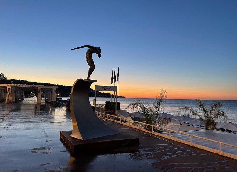 A sculpture of a bird on a curved structure by the waterfront at sunset. 5