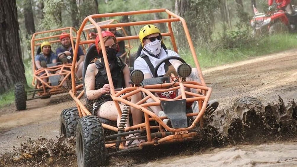 People in orange off-road vehicles on a muddy trail. 4